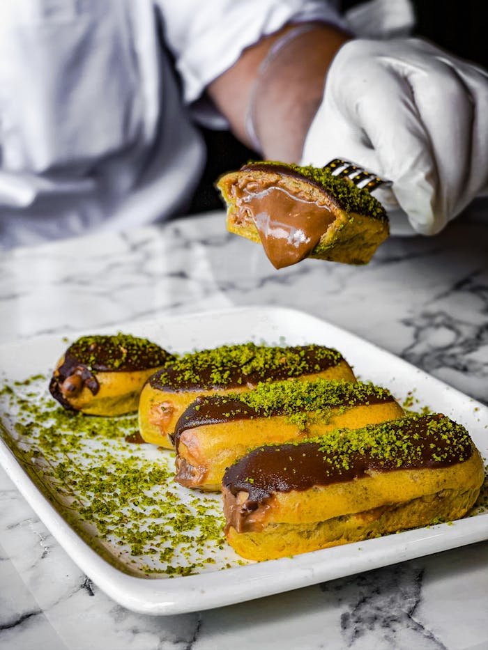 Close-up of chocolate eclairs with pistachio topping on marble table, perfect for dessert lovers.